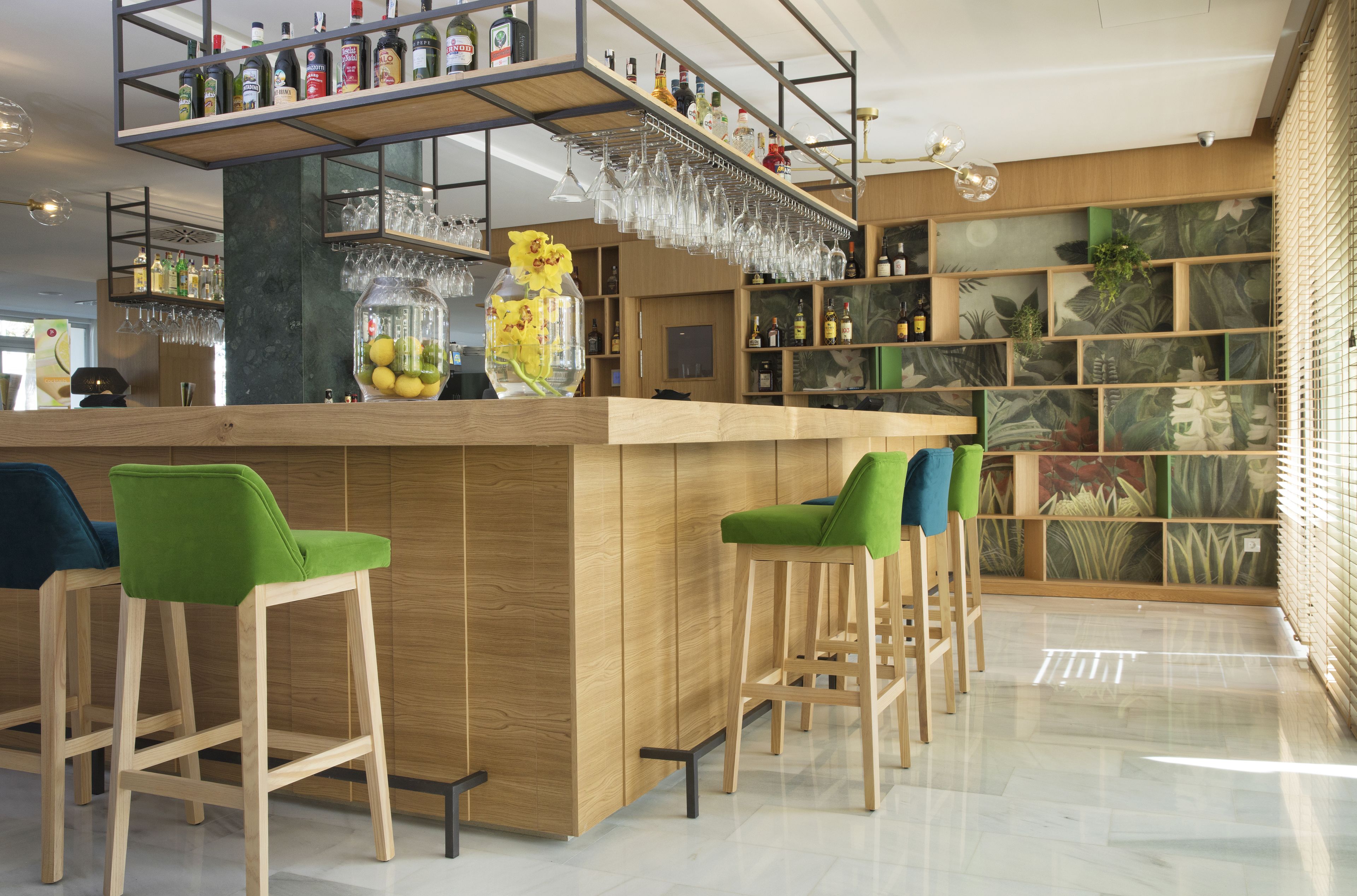 Un área de bar moderna con taburetes de madera, una barra y estantes llenos de botellas y vasos.