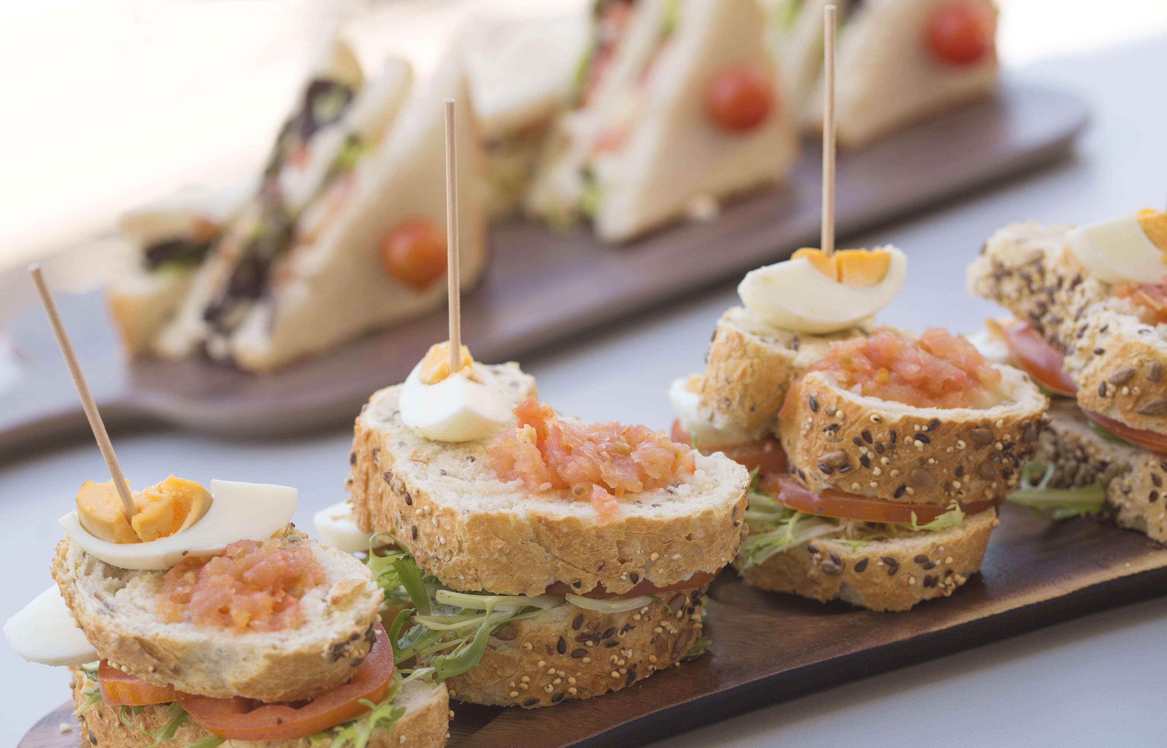 A variety of sandwiches with different fillings, including smoked salmon and eggs, arranged on a wooden board.
