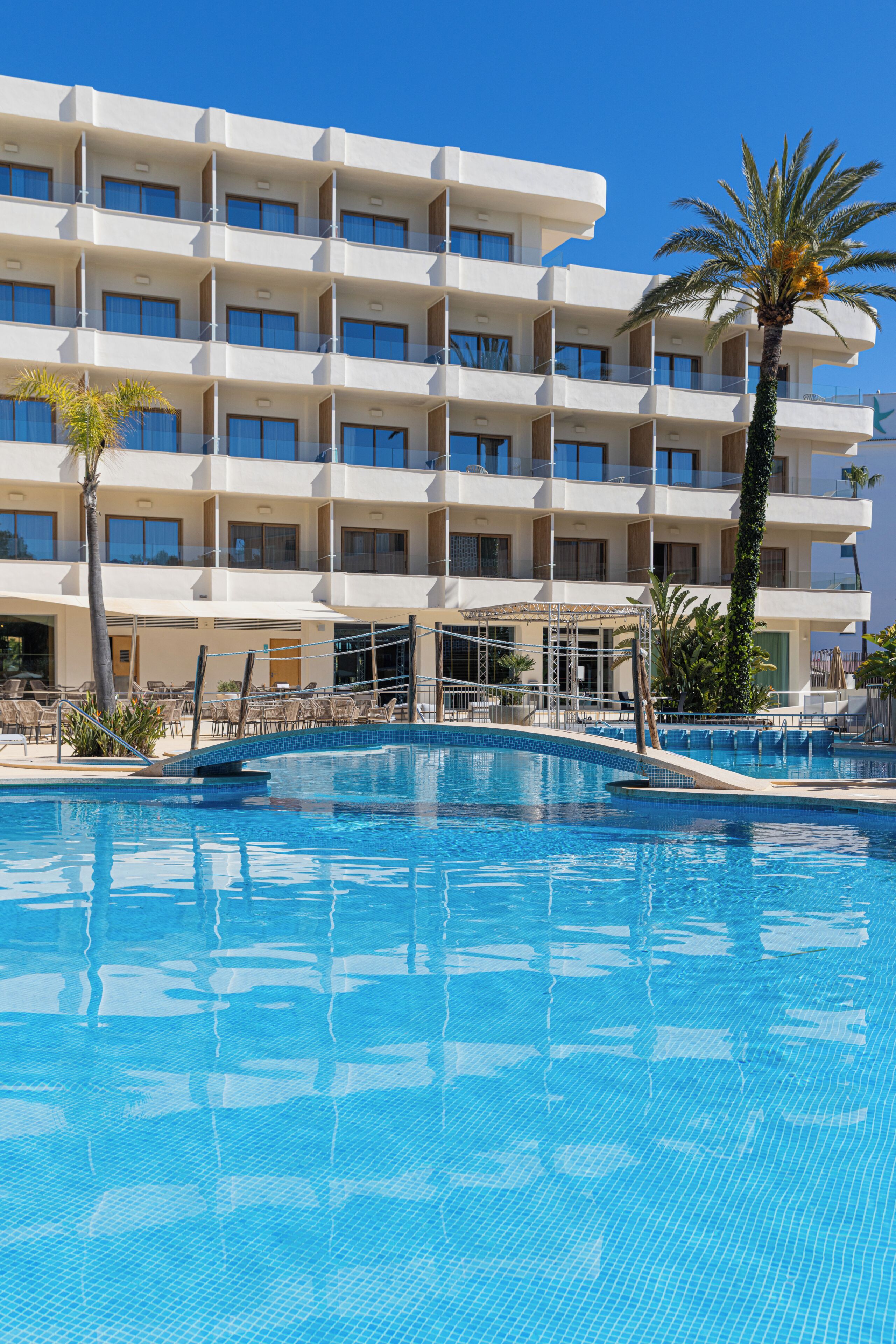 Een hotel met een zwembad, meerdere balkons en palmbomen.