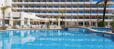 Un hotel con piscina, tumbonas y una palmera.