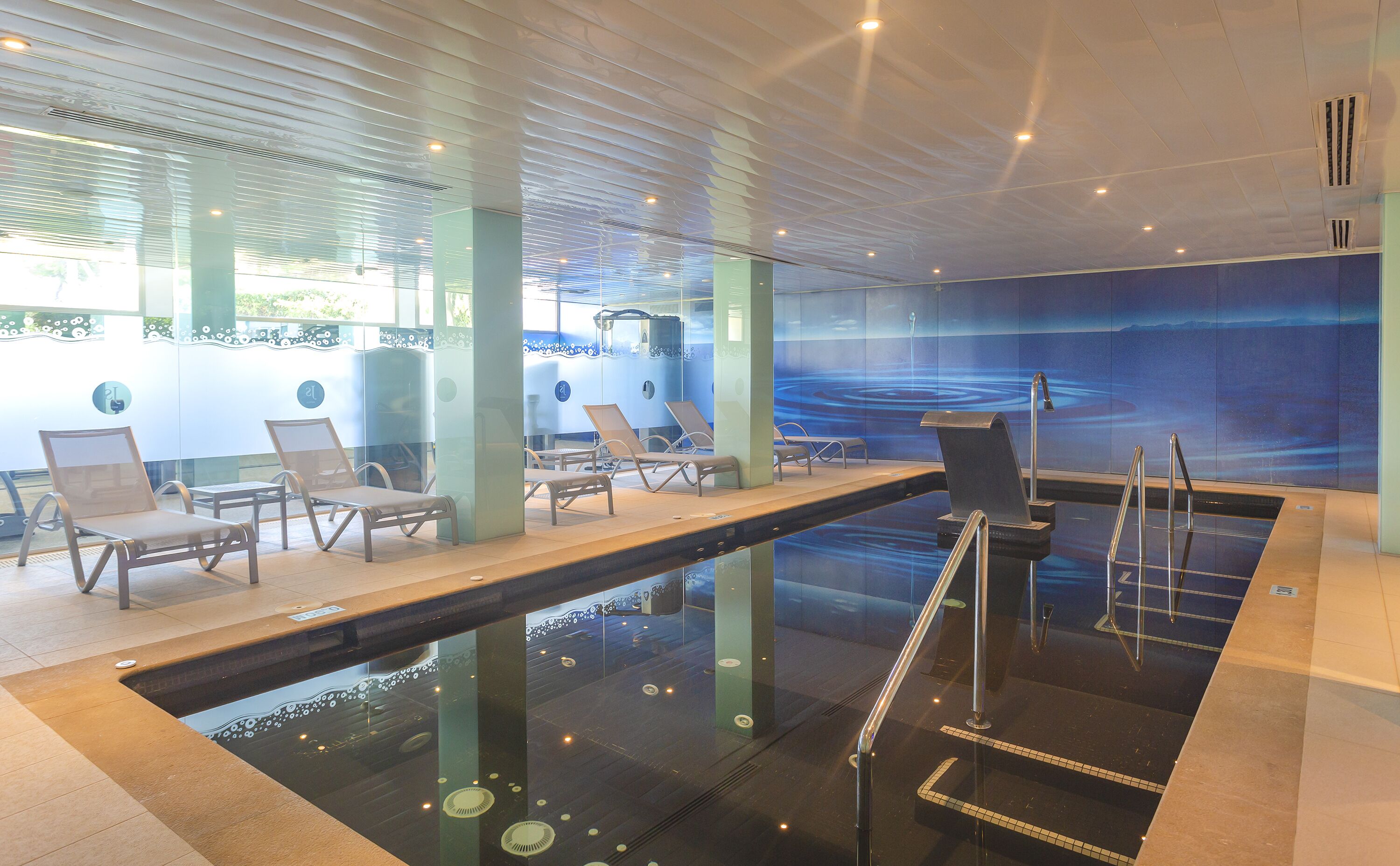 Un área de piscina interior moderna con sillones de descanso y una barrera de vidrio.