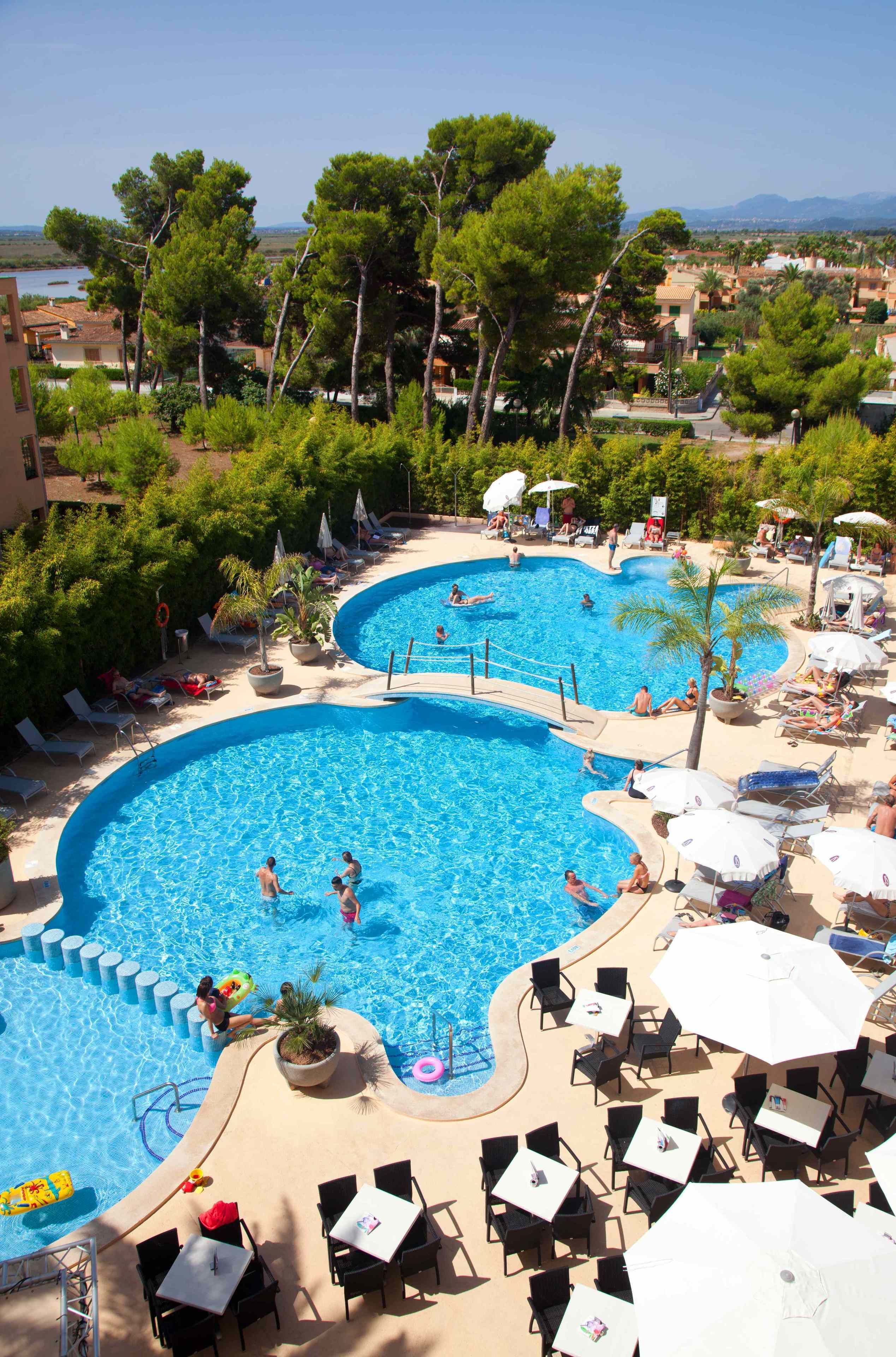 Una gran piscina al aire libre con varias secciones, rodeada de sillas de descanso y sombrillas, y árboles al fondo.