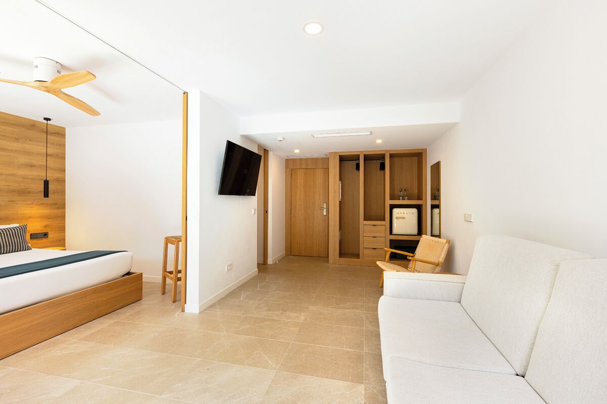 A modern bedroom with a wooden bed, a white sofa, a TV, and a wardrobe.