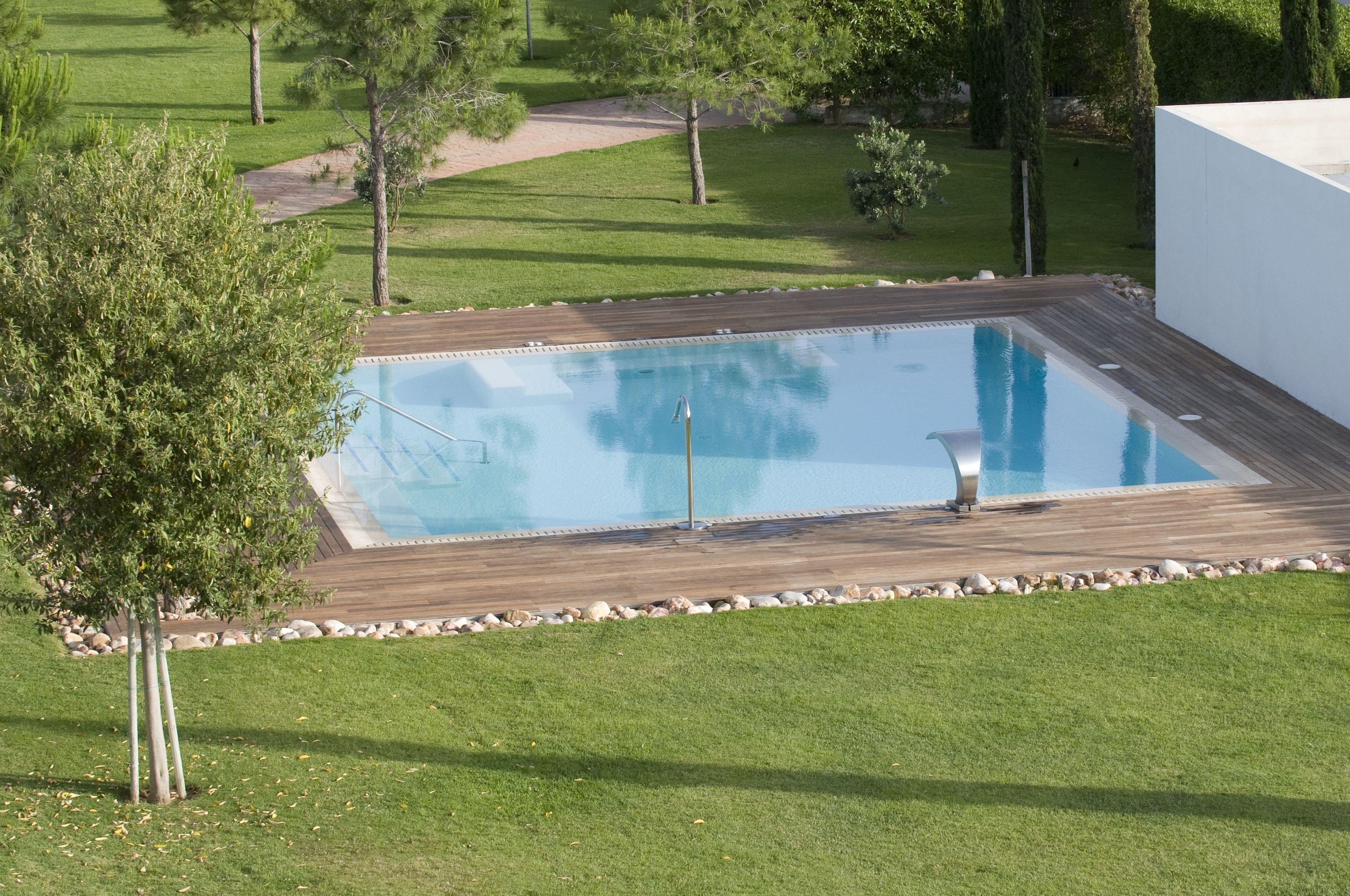 A rectangular swimming pool with a wooden deck, surrounded by a well-maintained lawn and trees.