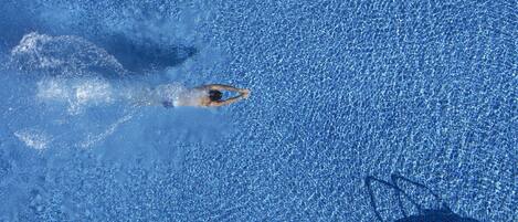 Eine Schwimmerin in einem Pool, deren Schatten durch eine Struktur geworfen wird.