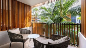 Un balcón con mobiliario de mimbre, una pequeña mesa redonda y vistas a palmeras y edificios.