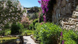 A stone pathway flanked by lush greenery and flowering plants, leading to a rustic building with a stone wall. - La Jacia Hotel & Resort (Arzachena)
