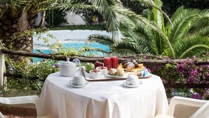 A round table with a white tablecloth, surrounded by white chairs, set outdoors with a view of a swimming pool and lush greenery. - La Jacia Hotel & Resort (Arzachena)