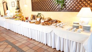 A buffet table with various food items and utensils, set against a tiled floor and a wooden lattice wall. - La Jacia Hotel & Resort (Arzachena)