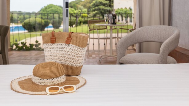 A room with a bed, a wicker basket, a straw hat, and sunglasses on the bed. - RVHotels Golf Costa Brava (Santa Cristina de Aro)