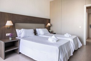 Ein Hotelzimmer mit zwei Betten, Nachttischen mit Lampen und einer kleinen Pflanze auf dem linken Nachttisch.