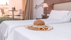 A hotel room with two beds, a table with chairs, a lamp, and a hat with sunglasses on one bed. - RVHotels Golf Costa Brava (Santa Cristina de Aro)