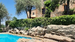 A pool with clear blue water, surrounded by large rocks and greenery, with stone buildings in the background. - Borgo Livernano (Radda in Chianti)