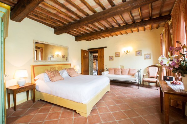 A bedroom with a large bed, a wooden ceiling, a sitting area with a sofa and armchairs, and a desk with a laptop. - Borgo Livernano (Radda in Chianti)