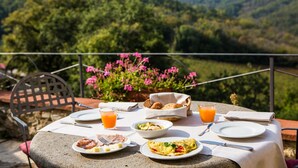 A table set for breakfast with plates, cutlery, and a basket of bread, overlooking a scenic landscape with hills and flowers. - Borgo Livernano (Radda in Chianti)