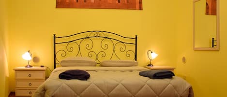 A bed with a headboard, two bedside tables, a wall-mounted mirror, and a painting above the bed.