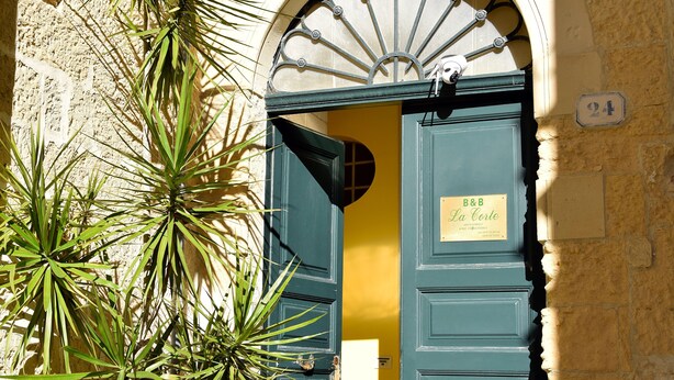 L’entrée d’un immeuble se distingue par une porte verte, une enseigne indiquant « B&B La Corte » et le numéro « 24 » peint sur le mur.