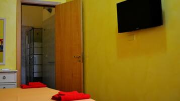 A hotel room with a bed, a wooden door, a shower area, and a mounted TV.