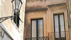 A building with a stone facade, a black metal balcony railing, and a traditional black door with a window above it. - La Corte Bed & Breakfast (Lecce)