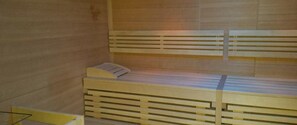 Una habitación pequeña con cama individual, paredes con listones de madera y un banco al pie de la cama.