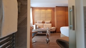 A modern hotel room with a wooden headboard, a sofa, a dining table, and a small dog figurine. - Vergeiner (Seefeld in Tirol)