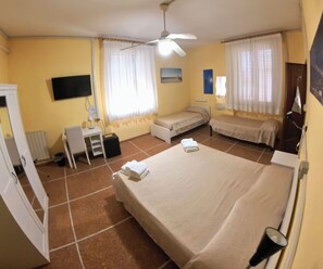Een hotelkamer met twee eenpersoonsbedden, een bureau met stoel, een televisie en een plafondventilator.