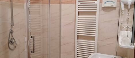 Un baño con ducha de vidrio, lavamanos blanco y toallero.