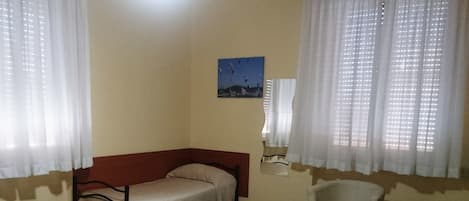 A room with two beds, a chair, a ceiling fan, and a painting on the wall.