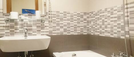 A bathroom with a white sink, a mirror, a shower, and a tiled backsplash.