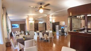 Un grand espace dédié à la salle à manger, avec plusieurs tables et chaises, un ventilateur de plafond et un téléviseur fixé au mur.