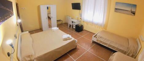 Quarto de hotel com cama, escrivaninha, cadeira, armário e janela com cortinas.