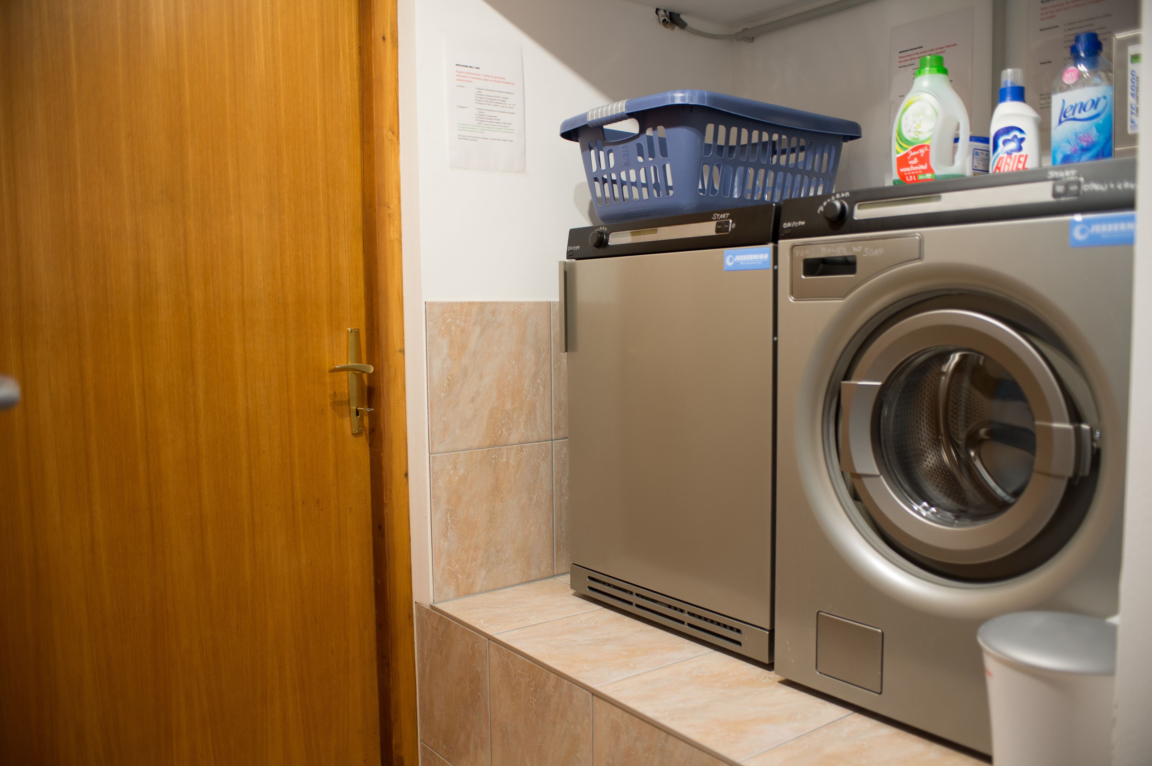 A compact laundry area with a washing machine and dryer, a blue laundry basket on top, and various detergent bottles.