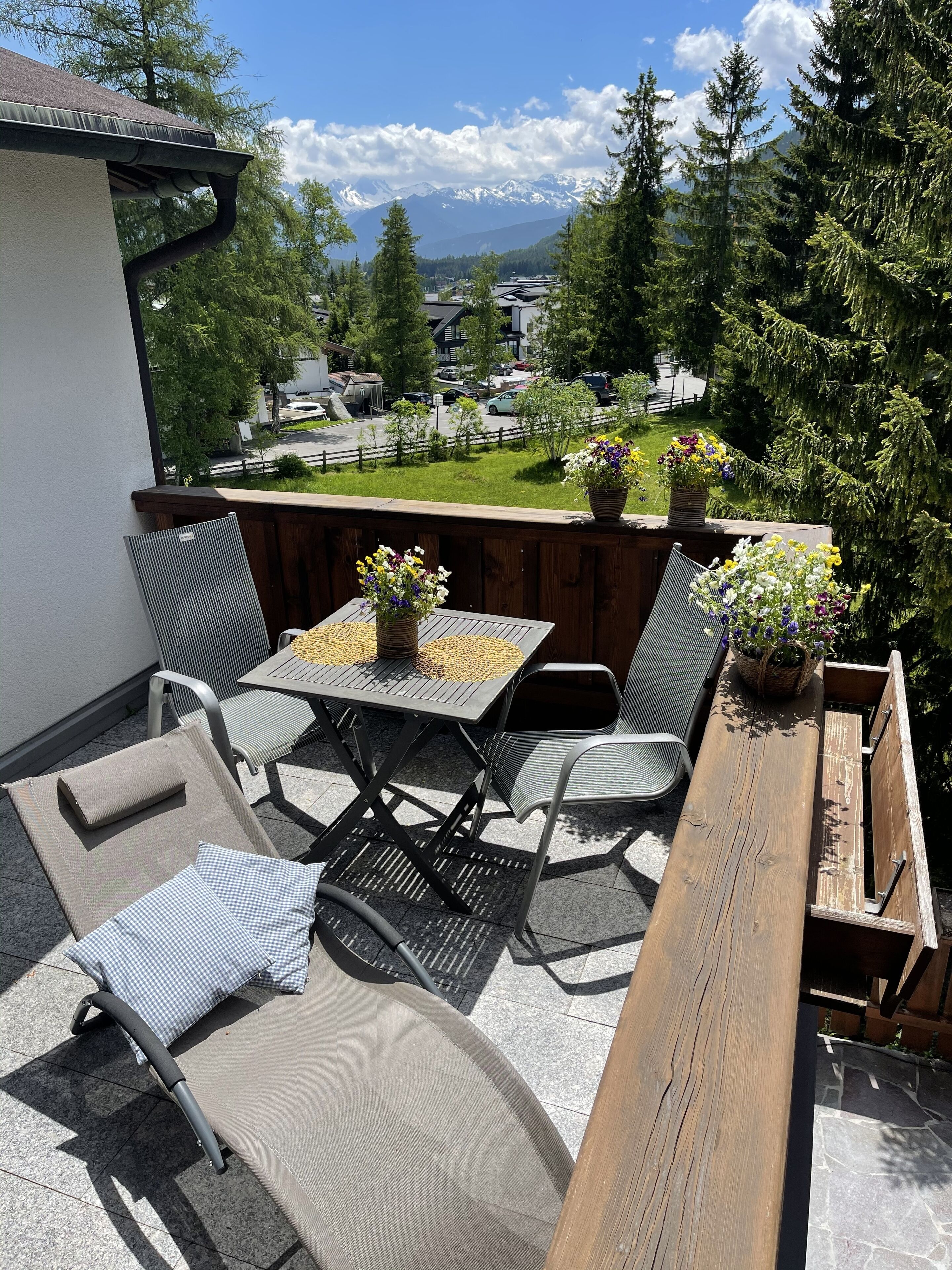 Une terrasse extérieure avec une table en bois, deux chaises et un banc. Des plantes en pot sont disposées sur la table.