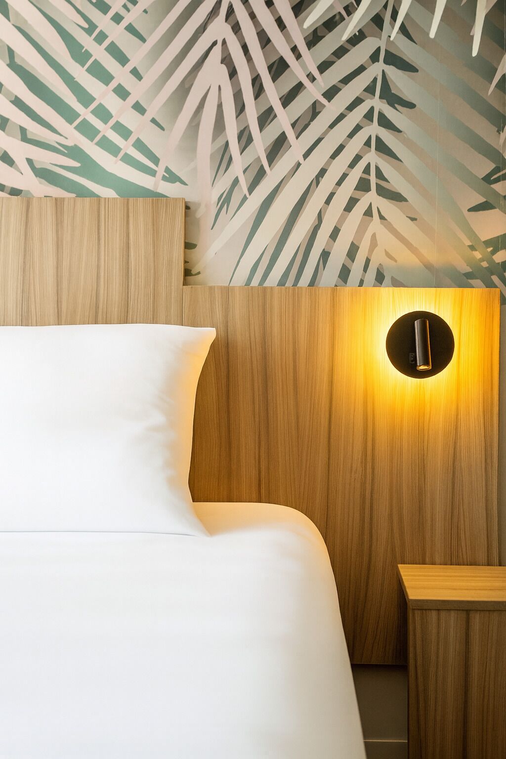 A bedroom with a wooden headboard, a white bed, and a nightstand with a circular light fixture.