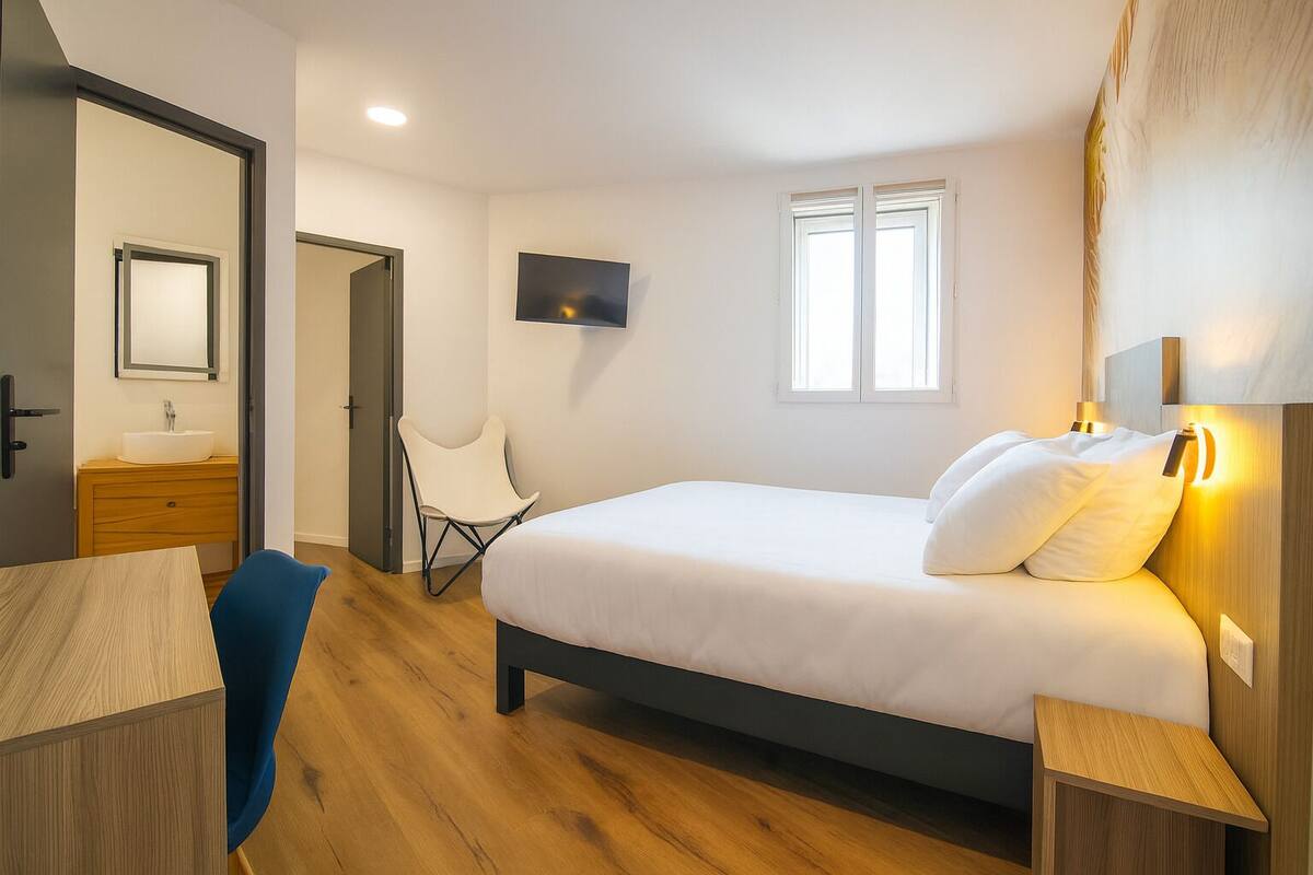 A bedroom with a bed, a chair, a TV, and a window.