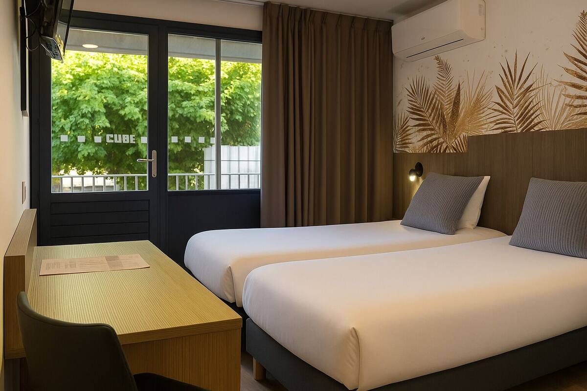 A hotel room with two beds, a desk, and a window with curtains.