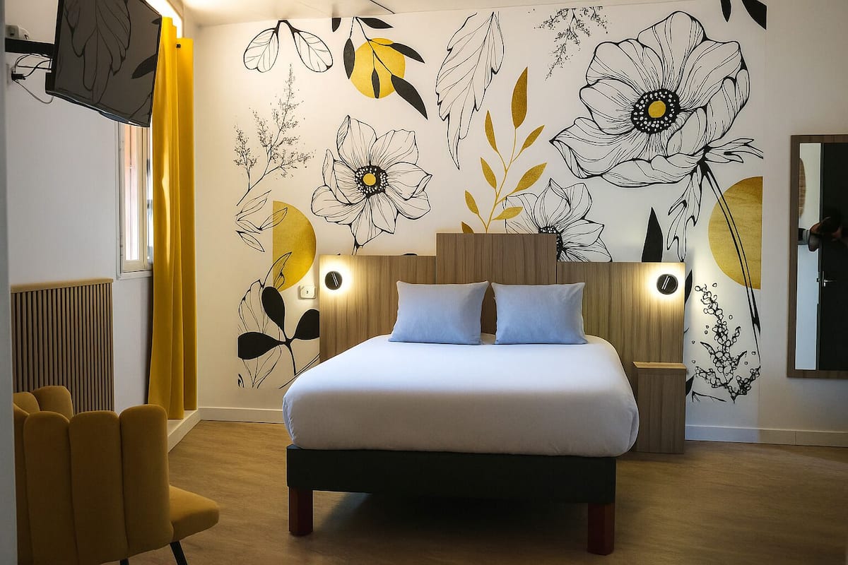 A modern bedroom with a large bed, two bedside tables with lamps, a TV mounted on the wall, and a yellow chair.