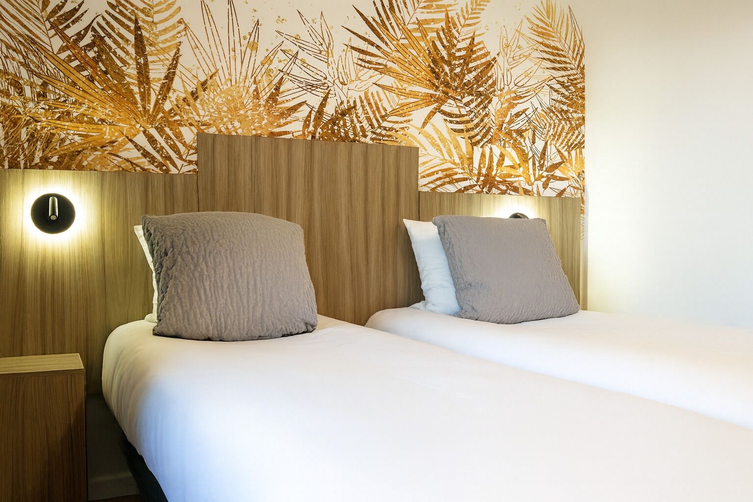 Een tweepersoonsbed met een houten hoofdbord en twee nachtkastjes, elk met een wandlamp.