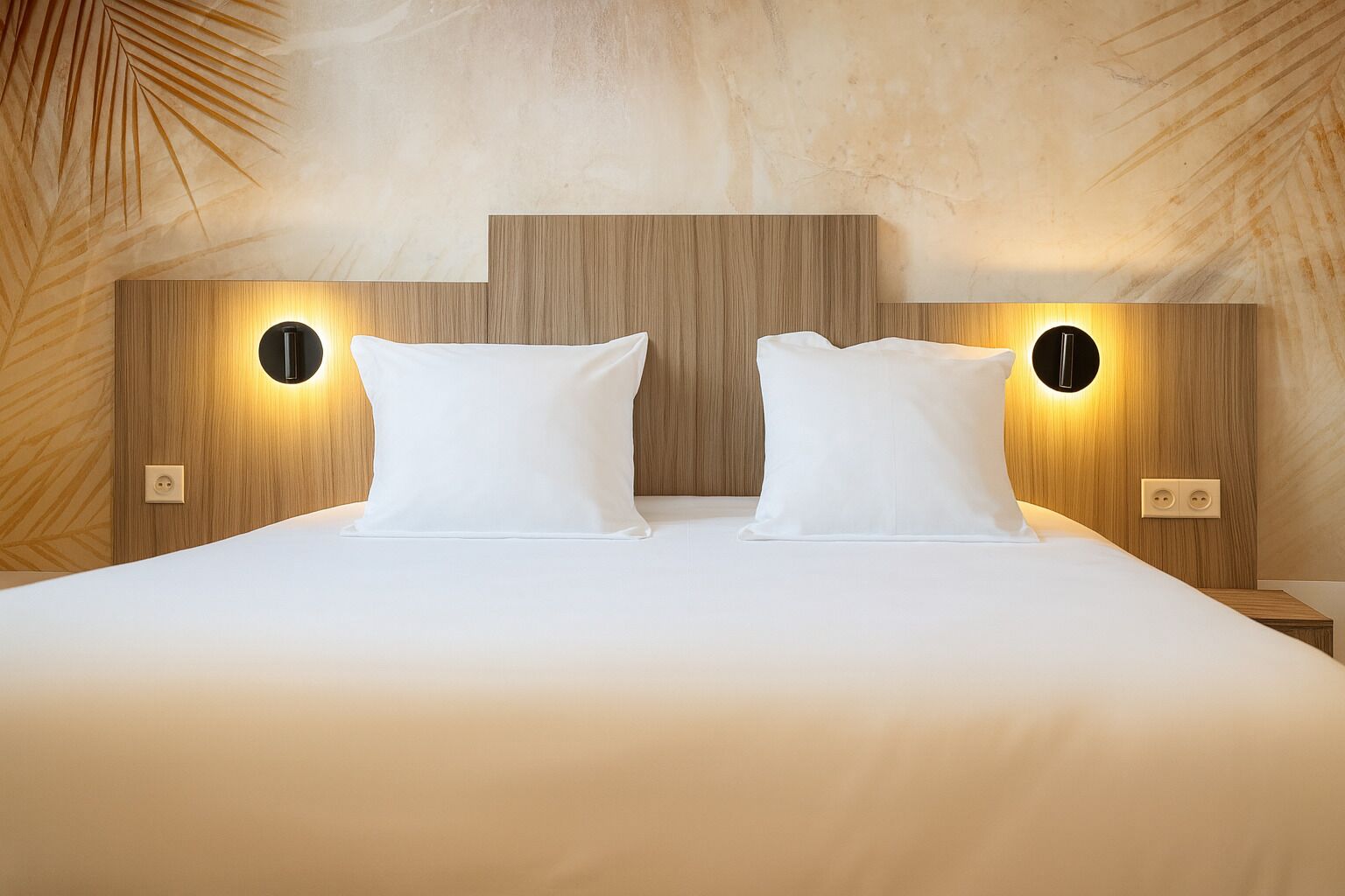 A hotel room with a large bed, two bedside tables, and wall-mounted lighting.