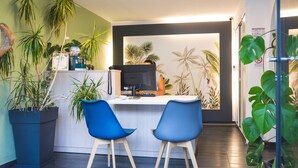 Een receptiebalie met twee blauwe stoelen, omringd door potplanten en een muur met behang van palmboompjes.