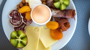Een ontbijtplateau met kaas, vleeswaren, fruit en een glas sinaasappelsap.