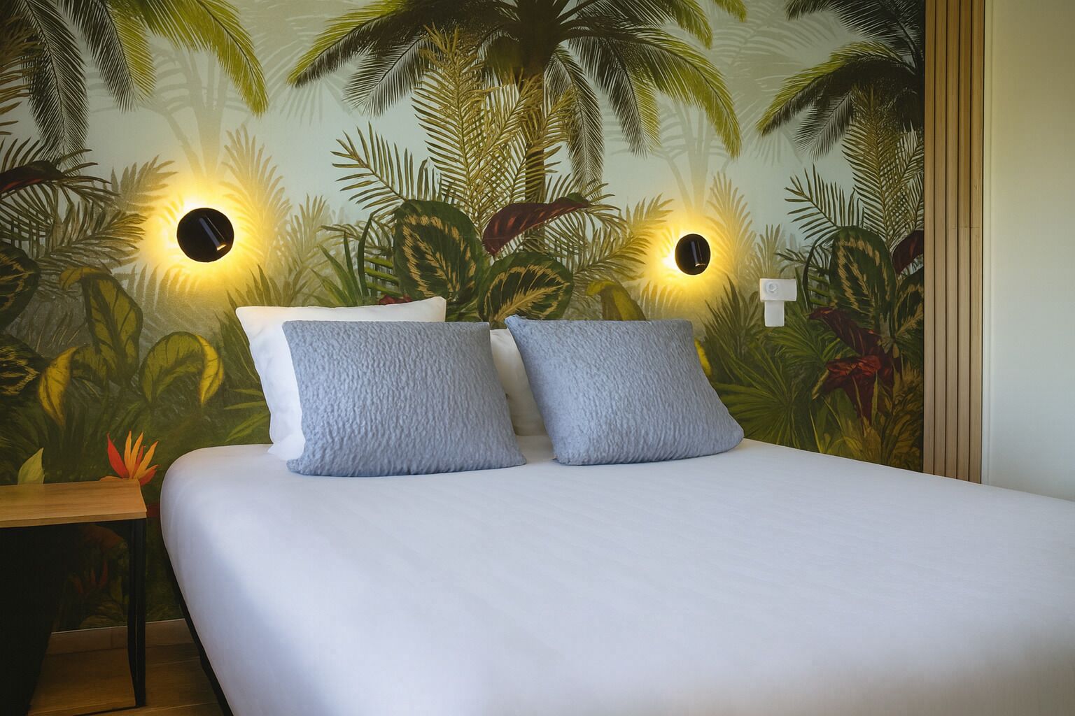 Un lit avec deux oreillers et une fresque murale représentant une végétation tropicale.
