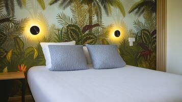 Un lit avec deux oreillers et une fresque murale représentant une végétation tropicale.