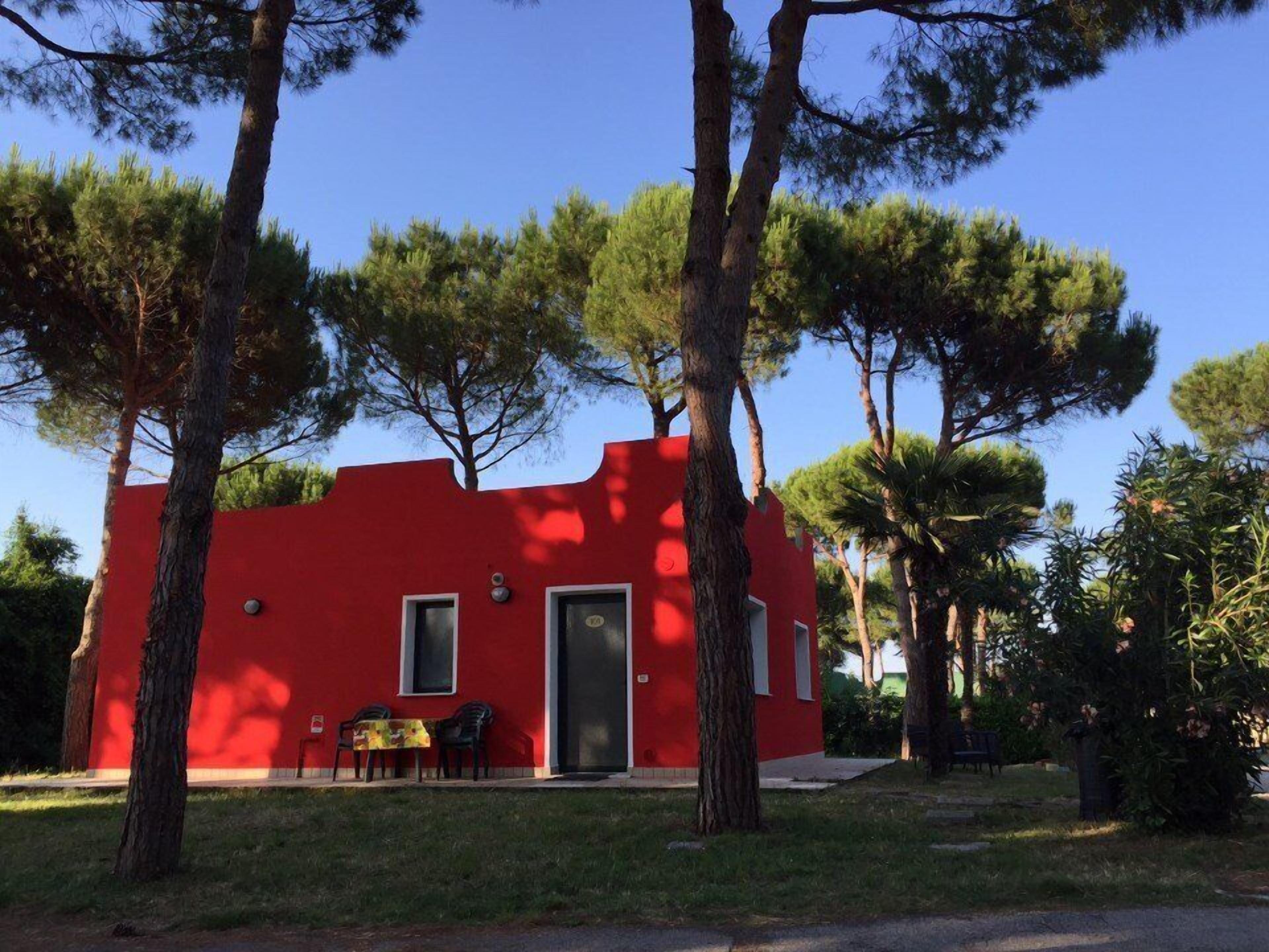 A red building with a door and windows, surrounded by trees and grass.
