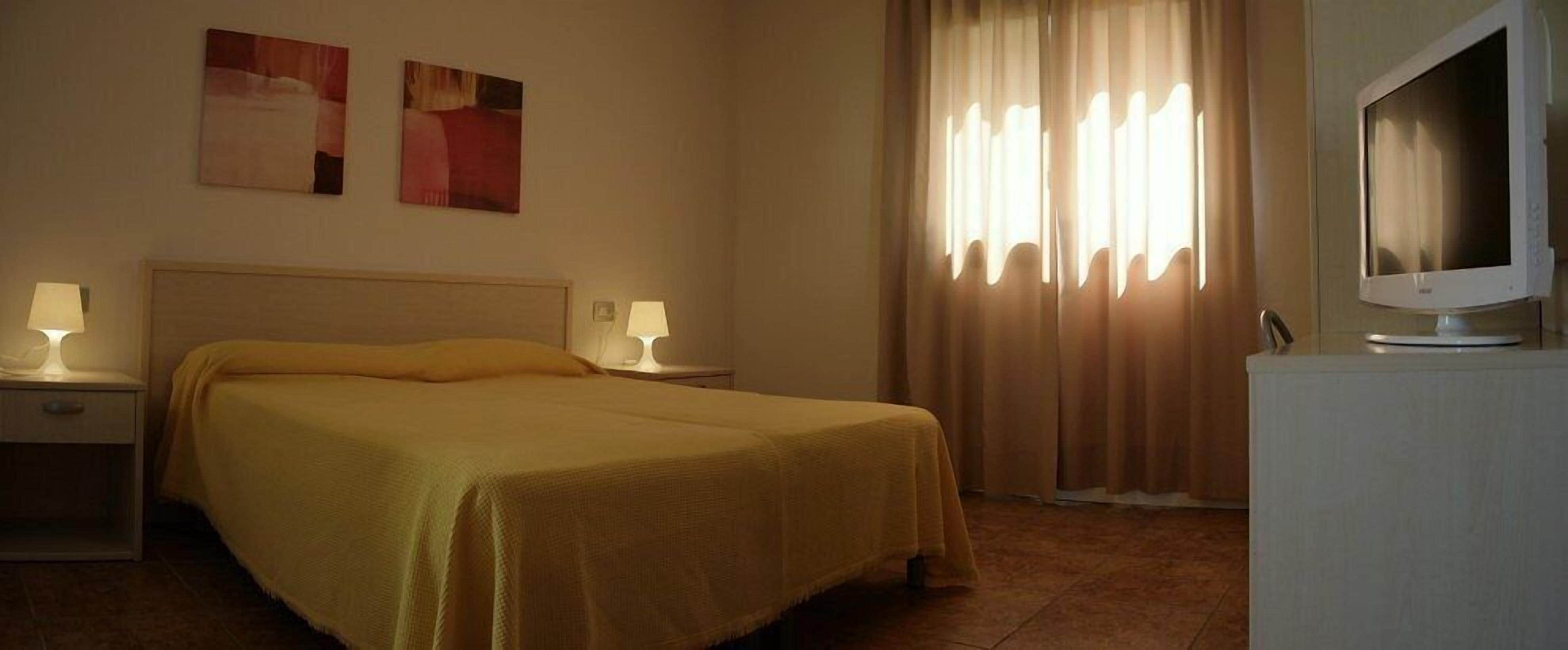 A hotel room with a bed, two bedside lamps, a flat-screen TV, and curtains.