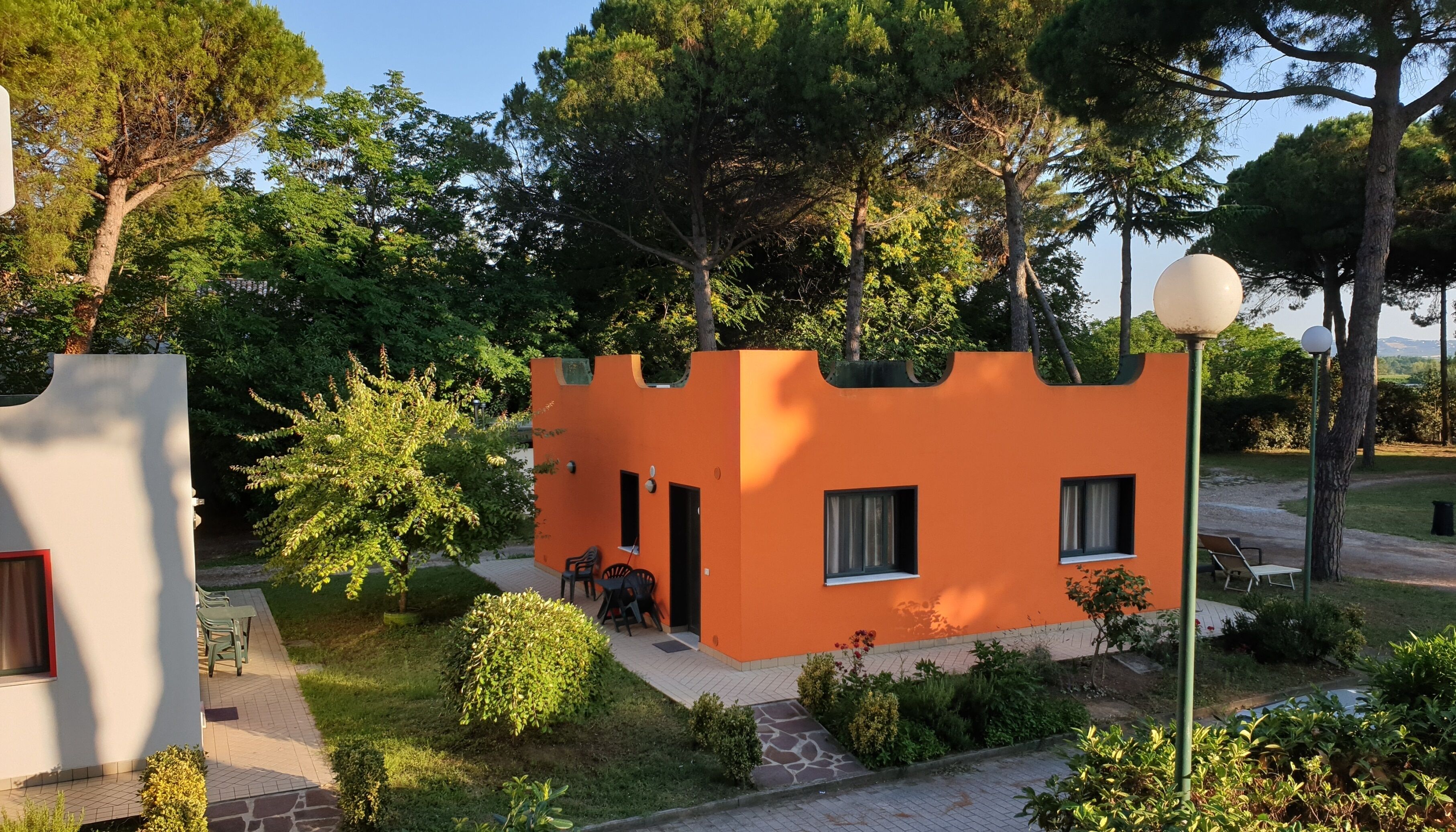 Un petit bâtiment orange, doté d’une seule entrée et de quelques fenêtres, entouré de verdure et d’arbres.