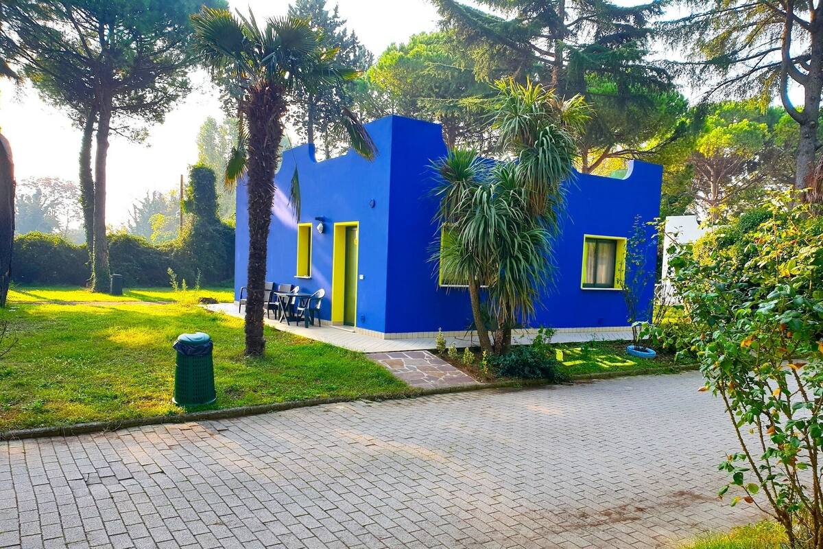 Un edificio azul con puertas y ventanas amarillas, rodeado de vegetación y un camino pavimentado.