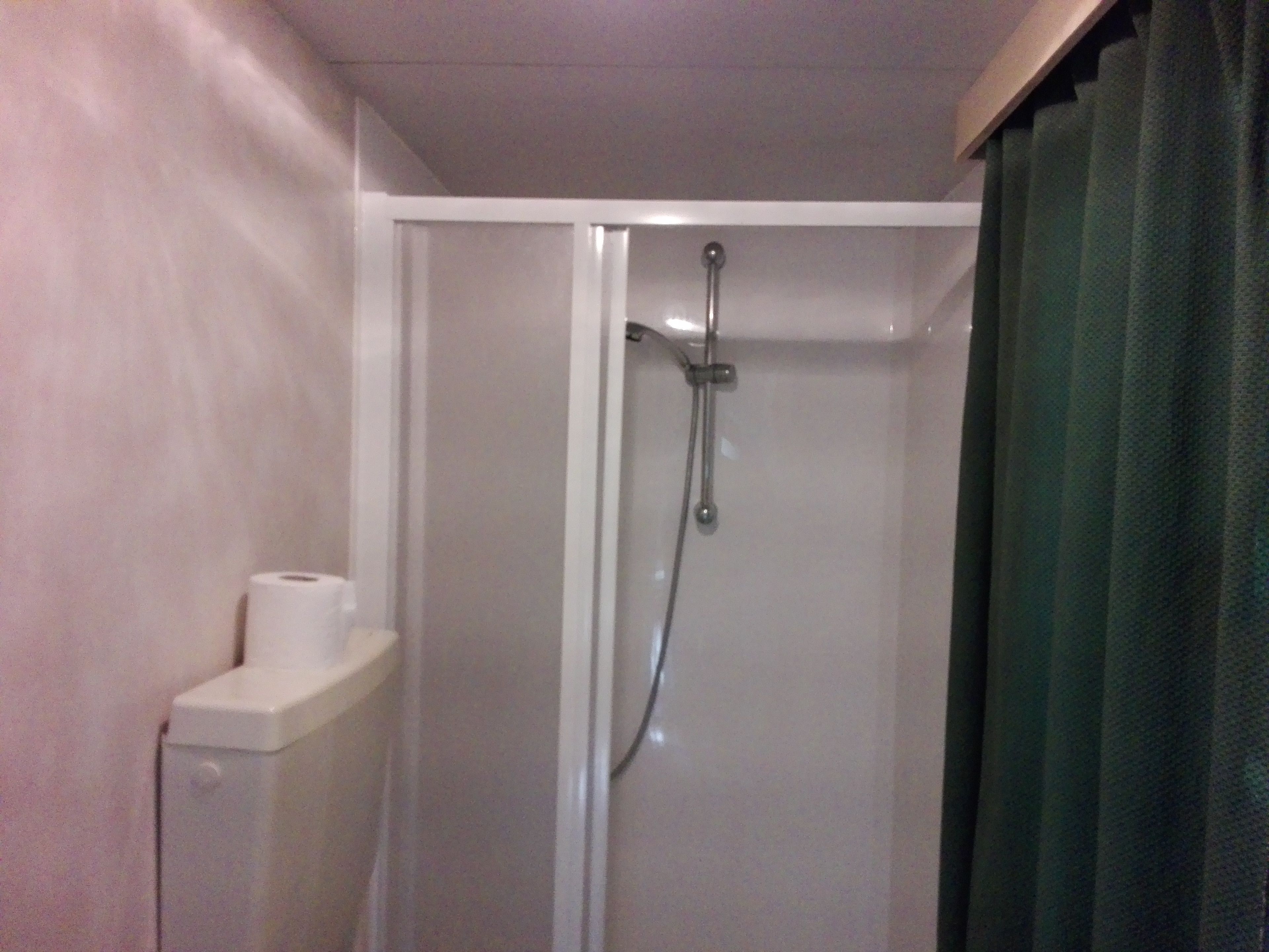 Une douche avec une porte en verre, un distributeur de serviettes et un rideau.
