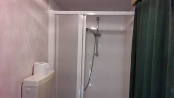 Une douche avec une porte en verre, un distributeur de serviettes et un rideau.