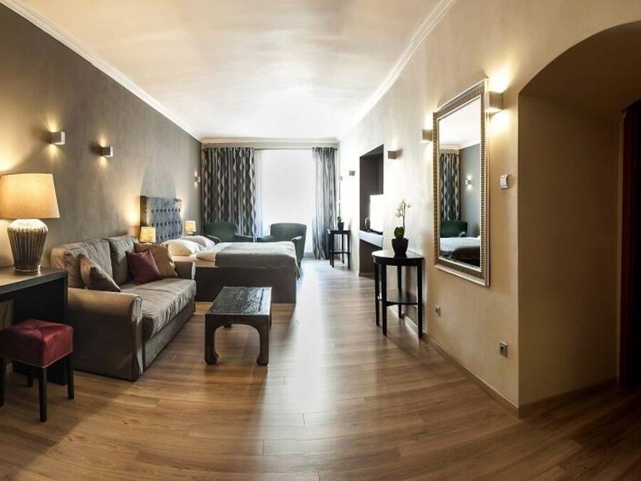 Een moderne hotelkamer met een bank, twee fauteuils, een salontafel, een bureau met lamp en een spiegel.